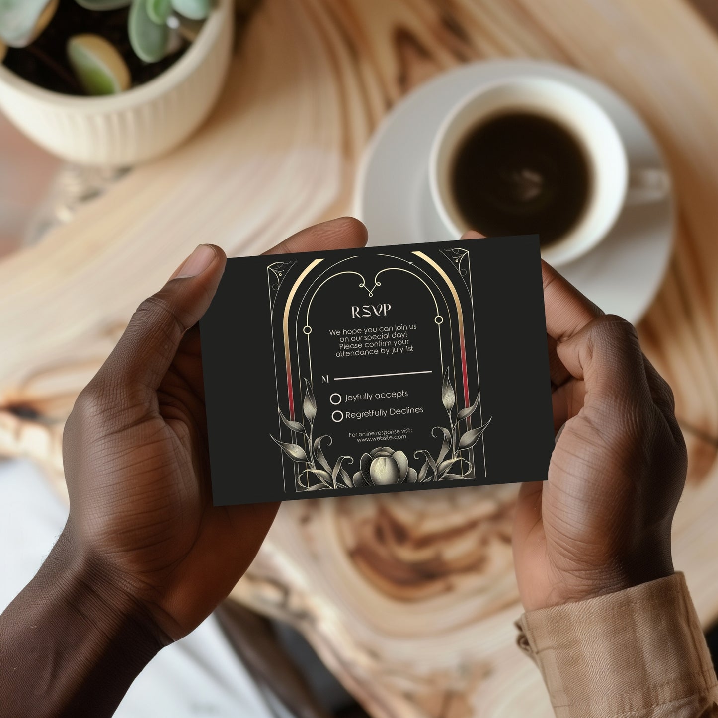 Person holding a black RSVP card with decorative gothic flower elements on a wooden table with a cup of coffee.